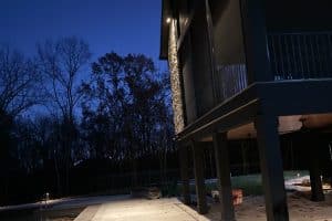 IMG_6914 | LandCo Group Modern house on stilts at dusk with a covered patio; construction materials and a toolbox on the ground, leafless trees in the background.
