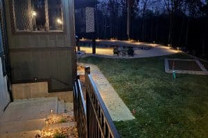 IMG_6916 | LandCo Group Nighttime backyard view: a lit pool, patio seating, and a house with concrete steps and a black railing along a walkway.