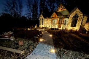 IMG_6917 | LandCo Group Nighttime view of a stone house with warm exterior lights; a lit concrete walkway leads to the entrance