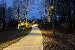 IMG_7026 | LandCo Group Curved concrete path illuminated by streetlamps winding toward a two-story house at dusk, bare trees on either side.