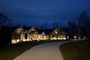 IMG_7032 | LandCo Group Nighttime exterior of a modern stone house lit by warm grounds lights along a curved driveway.