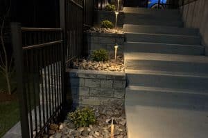 IMG_7034 | LandCo Group Nighttime outdoor stairway with concrete steps, stone planters, and small shrubs lit by solar pathway lights along the steps and rocky ground cover on both sides.