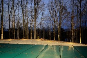 IMG_7035 | LandCo Group Night scene with a covered outdoor pool in the foreground, bare trees behind a fence lit by ground lights.