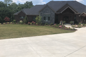 Brick house with stone accents, covered front porch, and landscaped front yard with flowers and shrubs on a sunny day.