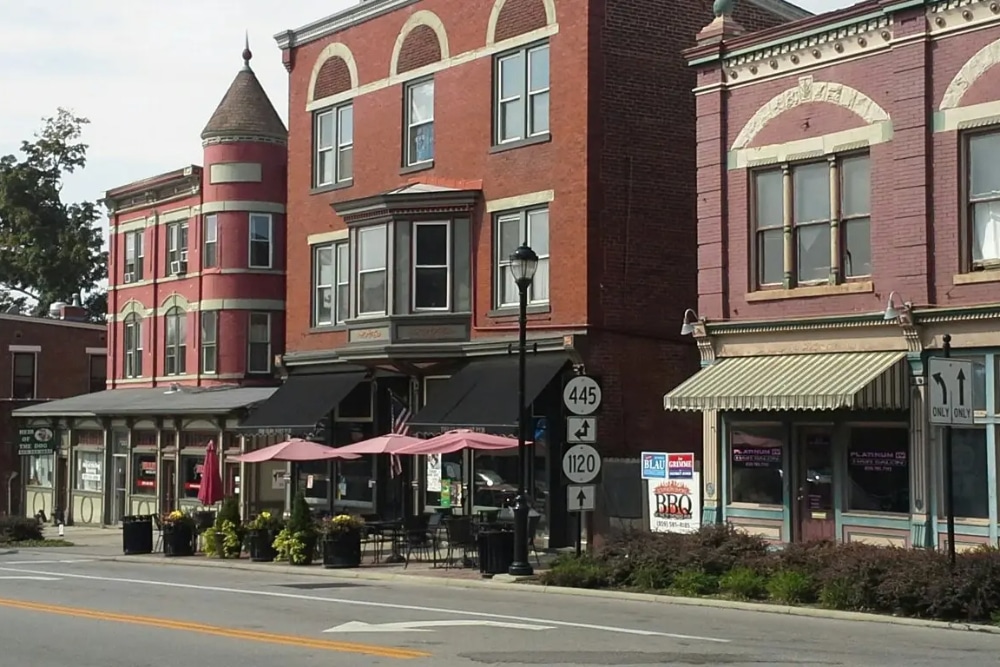 Fort-Thomas-Kentucky | LandCo Group Downtown street with red brick storefronts, outdoor seating under pink umbrellas, and a lamppost in front.