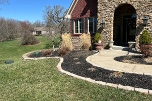 Front yard and house entrance with curved walkway, arched stone entry, and landscaped mulch beds along the doorway.