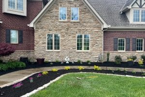 Stone-and-brick suburban house with landscaped front yard, curved concrete walkway, mulch beds, and small shrubs along the foundation.