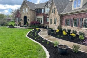 Front yard and grand entry of a two-story stone-brick house with a curved concrete path and mulched garden beds.