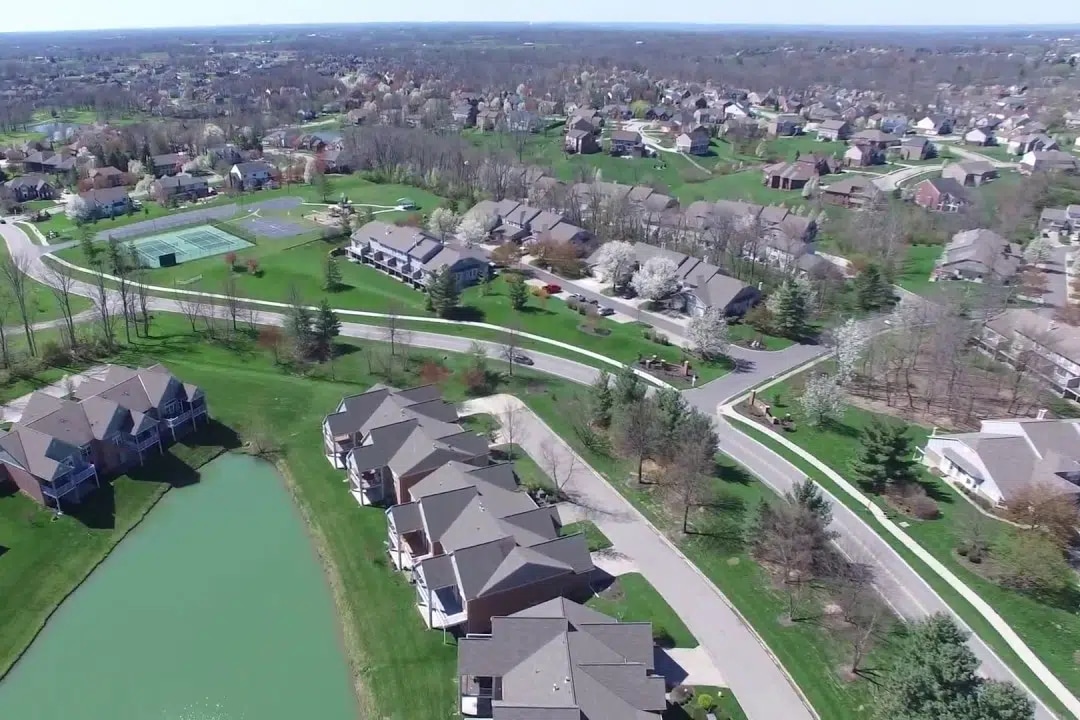 Union Kentucky | LandCo Group Aerial view of a suburban neighborhood with curved roads, townhomes along a pond, and green lawns under a clear sky.