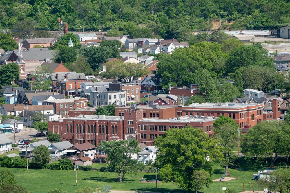 LudlowKY | LandCo Group Red-brick school building in a small town, surrounded by green trees and houses in the background.