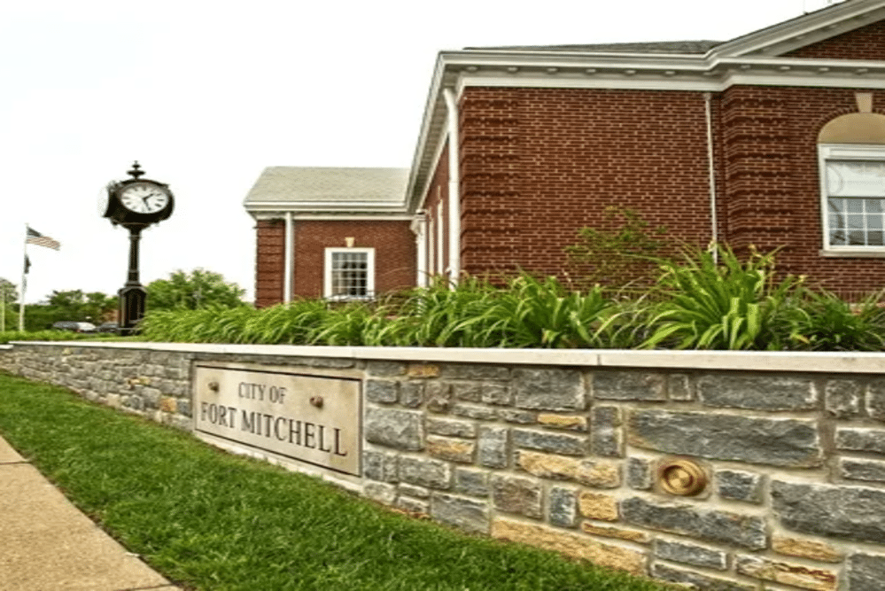 Fort Mitchell | LandCo Group City of Fort Mitchell sign on a stone wall beside a red brick municipal building and a vintage clock tower.