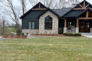 Union Full Landscape 1 | LandCo Group Front view of a modern house with stone and dark siding, wooden beams, and a covered porch, surrounded by a landscaped lawn.