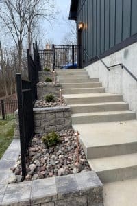 Union Full Landscape 12 | LandCo Group Concrete outdoor stairway beside a dark-green building with metal railings and rock-filled planters along the steps.