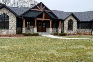 Union Full Landscape 2 | LandCo Group A modern stone-and-dark-siding house with a wooden front porch and steps leading to double doors, surrounded by a lawn and curved walkway.