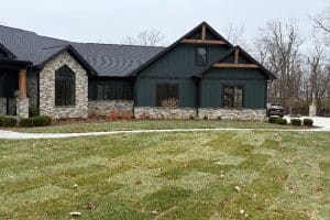 Union Full Landscape 3 | LandCo Group A modern dark-green house with stone accents, pitched roofs, and a manicured lawn with fallen leaves in front yard.