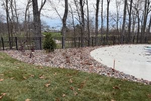 Union Full Landscape9 | LandCo Group Backyard landscape with a black metal fence, bare trees, and a rock-filled border surrounding a curved concrete patio area.